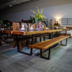 Solid Wood Furniture. Best wood furniture in Canada. Goweeraa. Wooden dining table with matching bench and chairs, decorated with plates, bowls, and a flower arrangement, set in a warmly lit showroom with other wooden furniture pieces in the background.